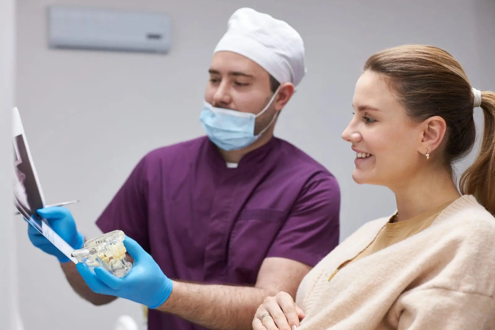 Stomatologist holds X-ray panoramic dental film and a plastic model of human jaw during consultation