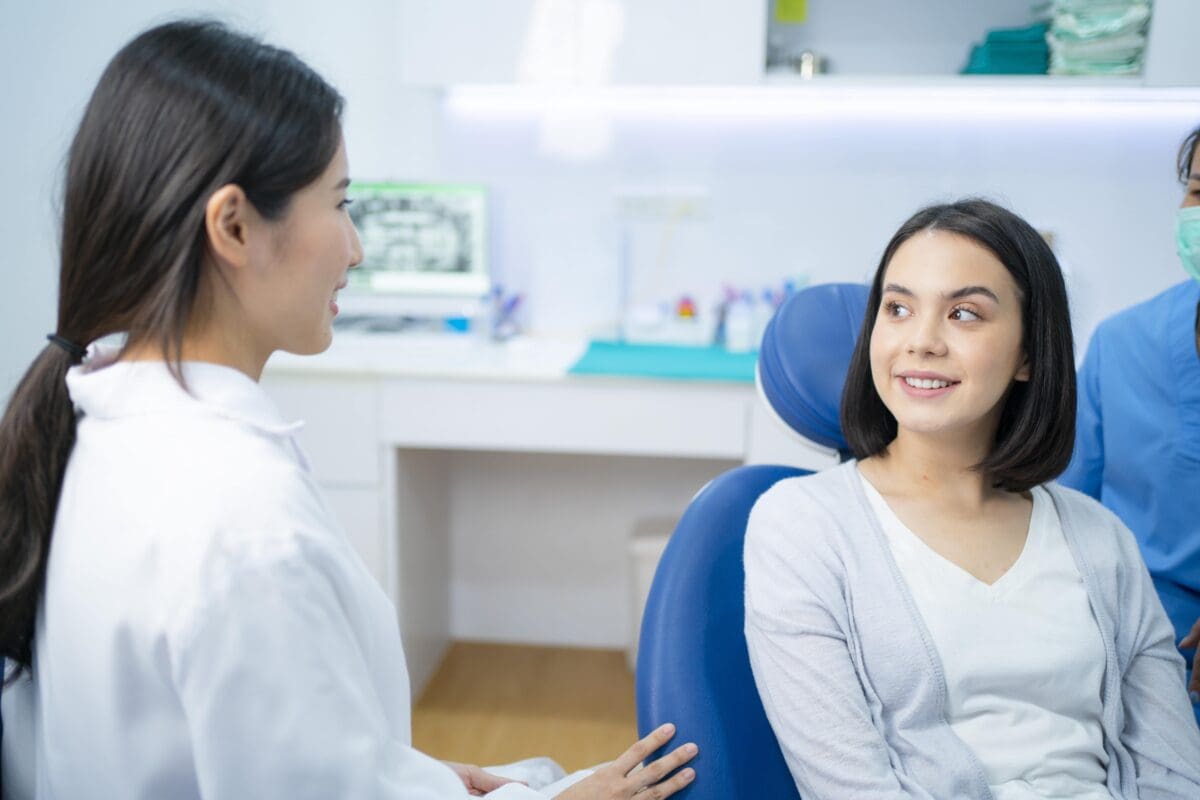 Caucasian girl talks and consult with dentist for cavities and gum disease in dental clinic.